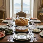 A festive table overflowing with traditional Easter food in Naples, featuring a savory Casatiello and a sweet Pastiera in the center.